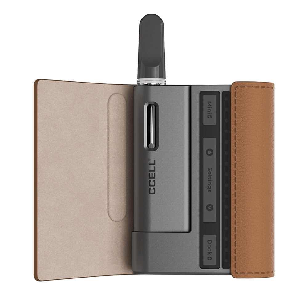 A detailed product shot of the CCELL Fino in Cocoa with Moon Gray. The rich brown faux-leather case is flipped open, revealing the gray power bank dock and the miniature battery base securely docked inside with a clear 510 oil cartridge fully attached and ready for action.