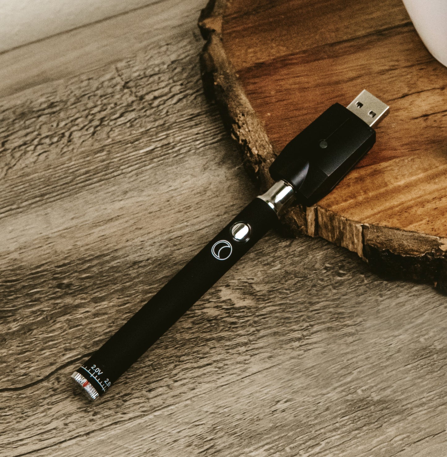 The Black Jane West Night battery with the geometric USB charger attached, resting on a natural wood table. This shot showcases the elegant contrast between the modern black device and the organic wood grain.