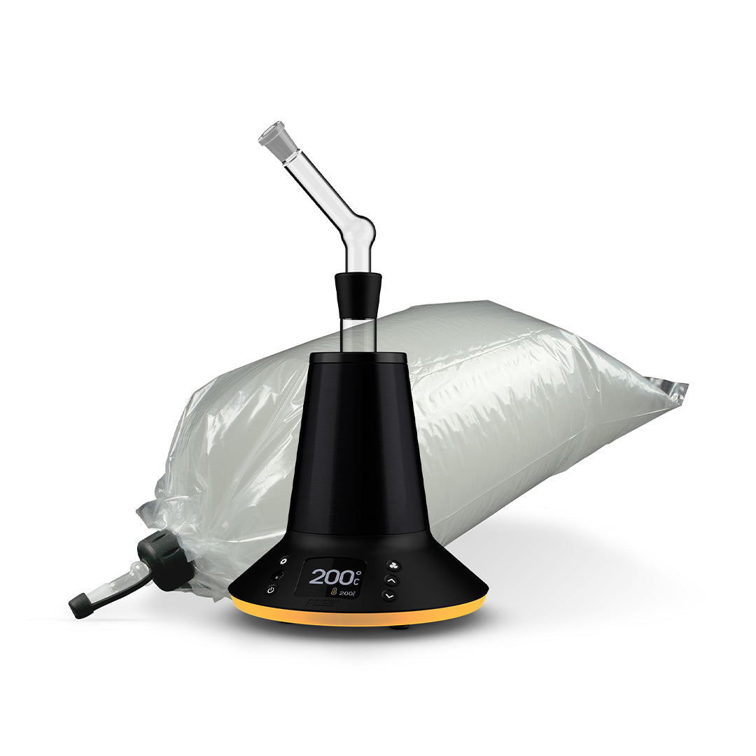A detailed studio product shot displaying the Arizer XQ2 arranged with its forced-air balloon attachment setup. The glass balloon connector is shown securely docked inside the top heating chamber of the midnight-chrome desktop vape, while a clear, high-capacity plastic balloon collection bag sits right next to the unit, highlighting its pre-installed glass balloon mouthpiece tip.