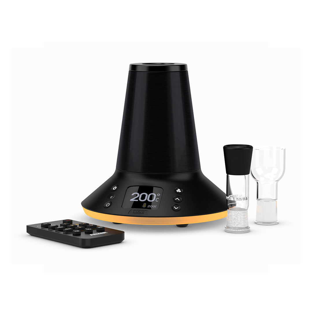 A comprehensive studio product layout showing the Arizer XQ2 Desktop Vaporizer standing alongside all its included box accessories. The midnight-chrome device is surrounded by the wireless remote control, two glass connoisseur bowls with silicone grips, an aromatherapy dish, a 3-foot silicone whip, glass balloon mouthpieces, pre-assembled balloon bags, replacement filters, a metal stirring tool, and the power supply unit on a clean background.