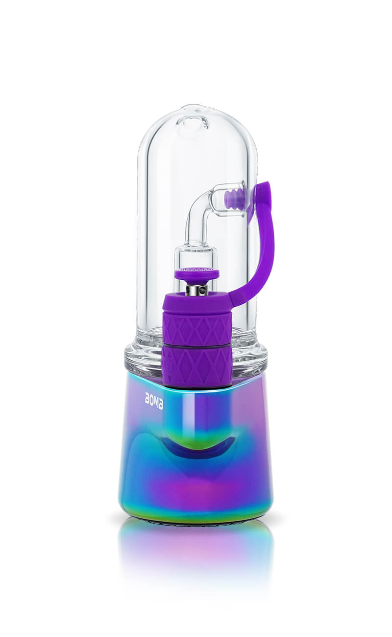 A front-facing view of the Rainbow Bomb Erig Aerix. This image highlights the symmetry of the device, showcasing the clear glass bubbler and the vibrant purple carb cap and purple airpath tube that provide a bold contrast against the rainbow metallic base.