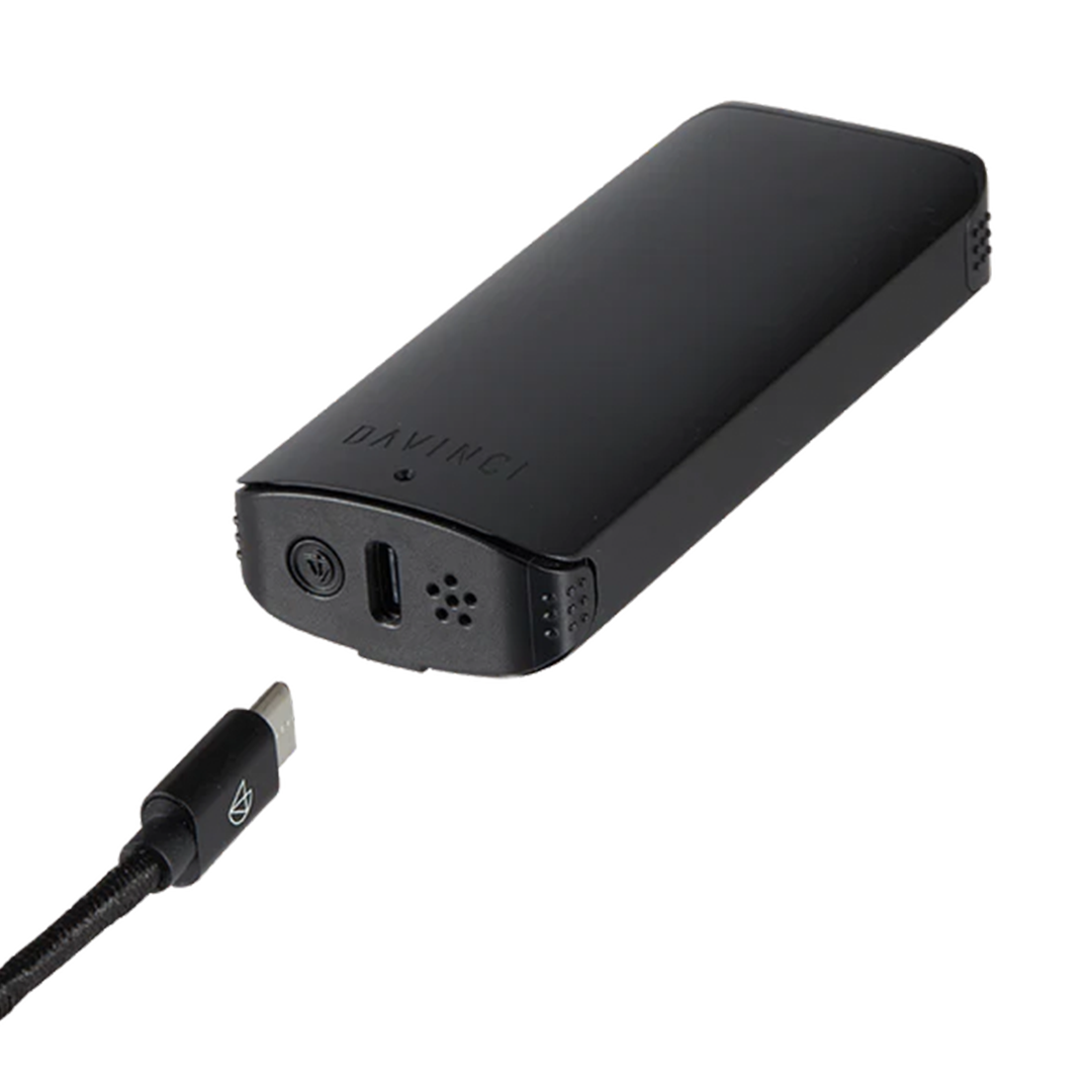 A detailed product utility shot of the Onyx Black DaVinci ARTIQ laid horizontally. A black USB Type-C charging cable is shown plugging directly into the dedicated fast-charging port located on the flat base of the device, illustrating convenient and upright-friendly power management.