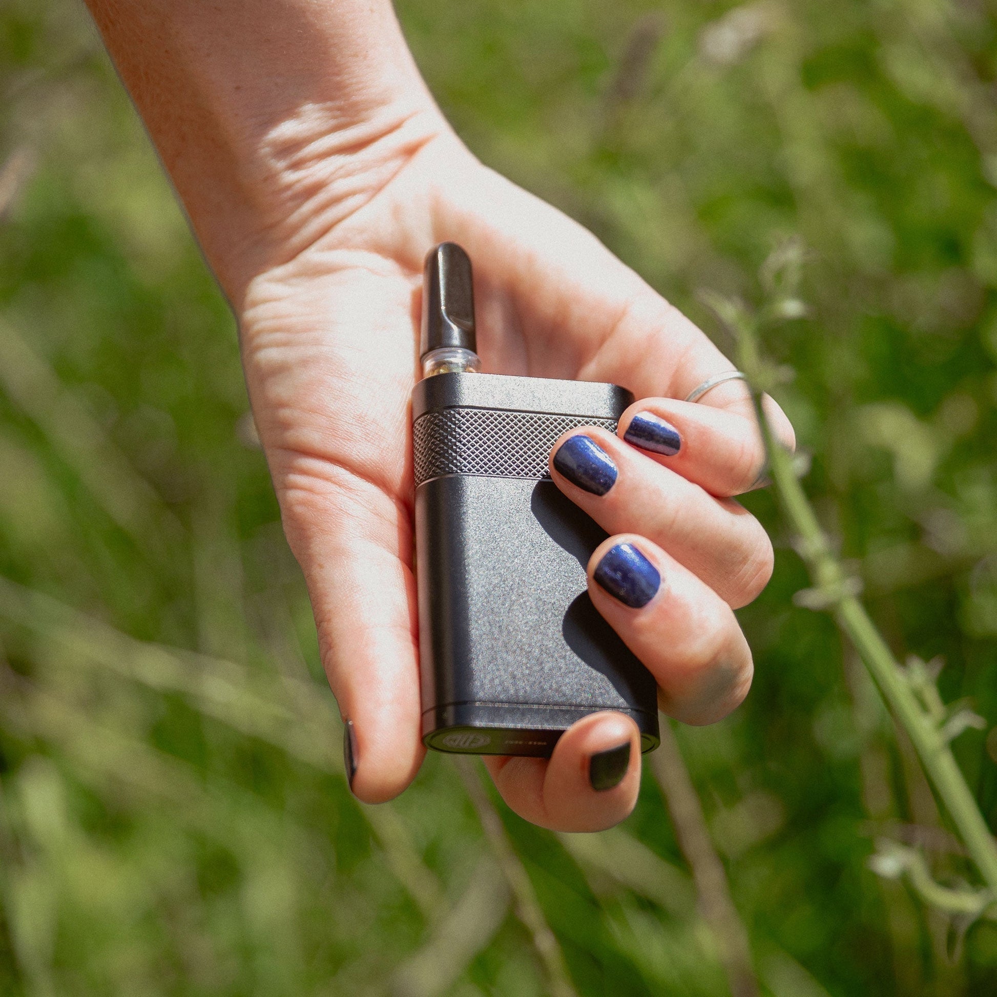 A lifestyle image of the Everyday Canna Co. Ranger being held in a hand with a 510-thread cartridge installed. Set against a soft-focus natural green background, this photo demonstrates the compact, ergonomic size of the aircraft-grade aluminum battery in a real-world setting.