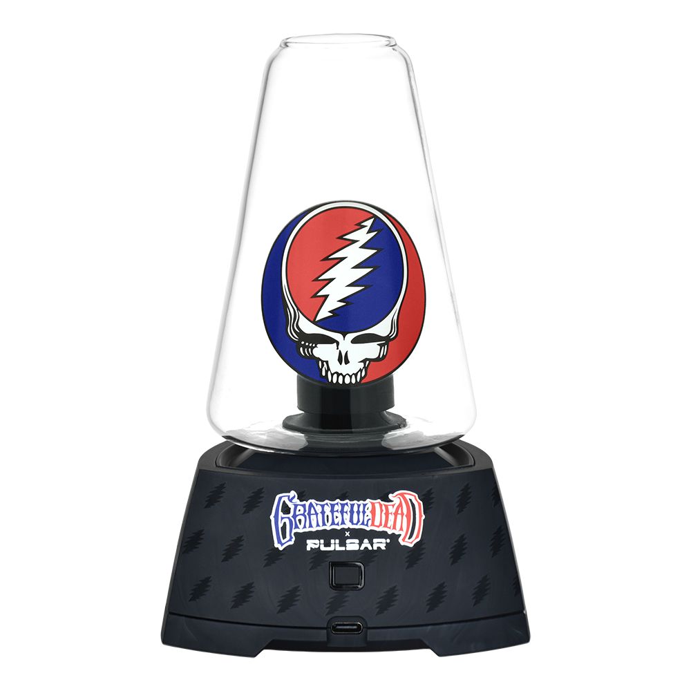 A clean front-facing studio shot of the Grateful Dead x Pulsar Sipper Vaporizer. The device showcases its premium black base textured with stylized lightning bolts and a clean central touchpad button, topped by the clear borosilicate glass dry cup attachment which cleanly exposes the colored 3D Grateful Dead Steal Your Face skull sculpture resting inside the center chamber.