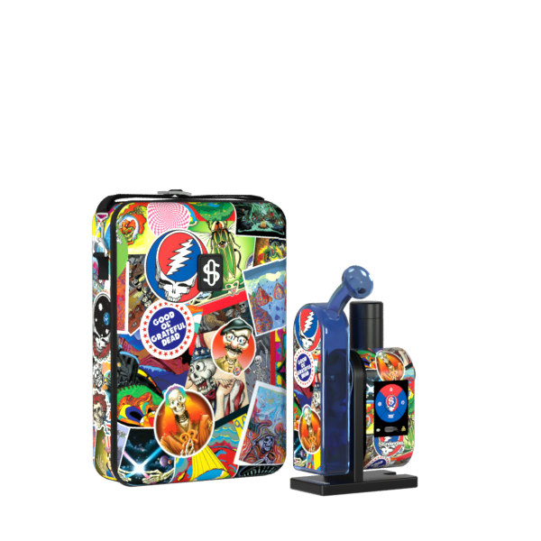 A front-angle studio product shot displaying the assembled Grateful Dead x Stündenglass Modül + Dok Legacy Patchwork device standing next to its matching hardshell travel case. The handheld glass e-rig station showcases vibrant, colorful Grateful Dead patchwork graphics wrapped around its base, perfectly complementing the heavy-duty zippered carrying case featuring identical iconic band imagery.