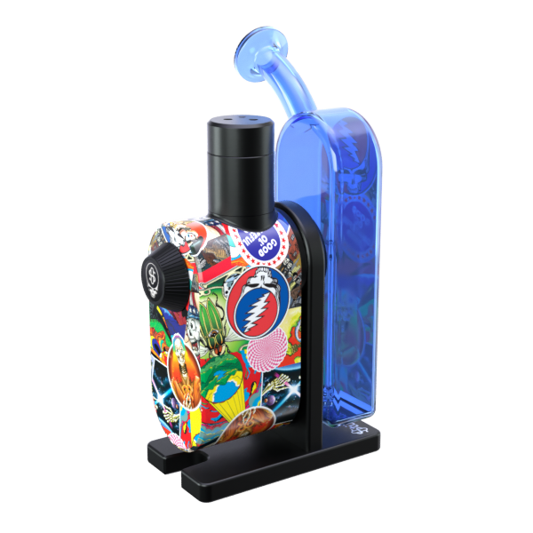 A crisp, rear-angle studio product shot of the assembled Grateful Dead x Stündenglass Modül + Dok Legacy Patchwork device. This perspective emphasizes the clean lines of the heavy-duty handheld docking frame, highlighting how the intricate, multicolored licensed band collage wraps seamlessly around to the back panel of the chassis beneath the clear glass globe.