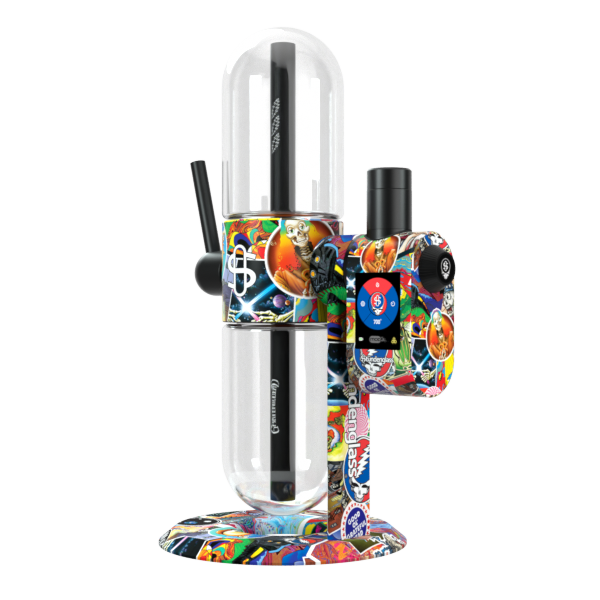 A crisp, front-angle studio product shot showcasing the Grateful Dead x Stündenglass Modül smart power base docked onto the full-sized Grateful Dead Gravity Infuser. The angle captures the bold profile of the complete glass setup, emphasizing the multi-paneled patchwork band imagery wrapped around the entire base assembly beneath the prominent rotating borosilicate glass globes.