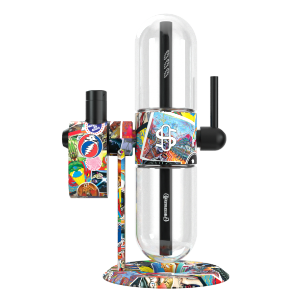 A clean, rear-facing studio product shot displaying the Grateful Dead x Stündenglass Modül smart power base mounted onto the back connector of the Grateful Dead Gravity Infuser. The perspective highlights the clean mechanical integration of the digital heating engine, showing how the colorful licensed patchwork artwork patterns flow fluidly across both premium hardware pieces.