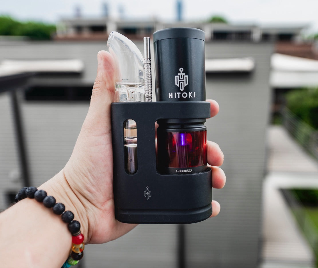 A lifestyle shot of the Hitoki Saber Portable Kit being held, demonstrating its compact and ergonomic design. The image shows the matte black finish and the central power button, emphasizing how easily the laser device fits in the palm of a hand for on-the-go use.