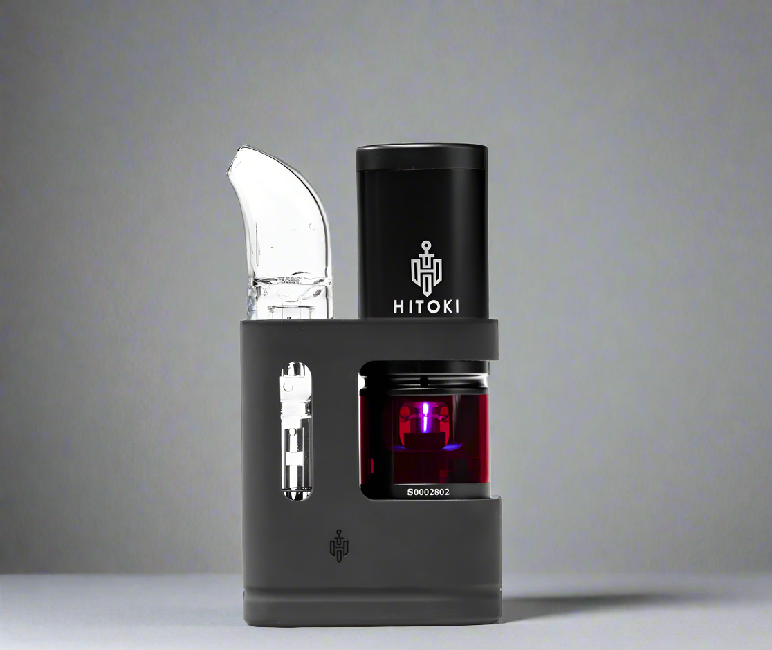 A clean side profile of the Hitoki Saber Portable Kit resting on a white surface against a neutral gray background. This shot highlights the elegant, cylindrical silhouette of the device and the seamless connection between the laser base and the portable attachment.