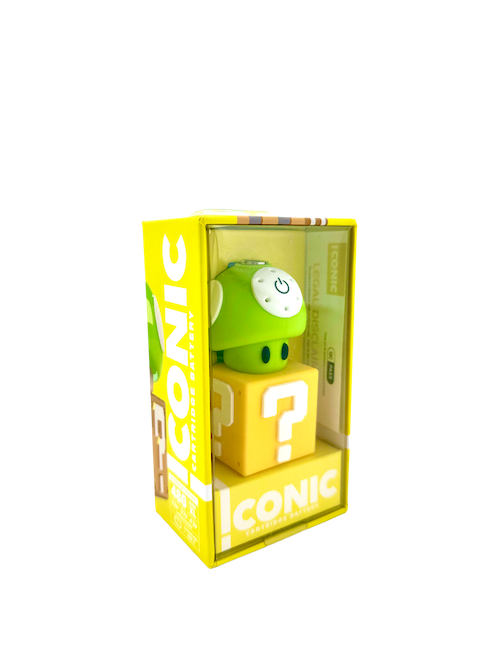 A crisp, front-facing studio product shot of the Iconic Mushroom Battery in Green displayed inside its official retail packaging. The device features a vibrant, high-gloss green cap with classic white spots sitting on top of a clean white stem base, securely nested inside a minimalist cardboard box with a clear display window.