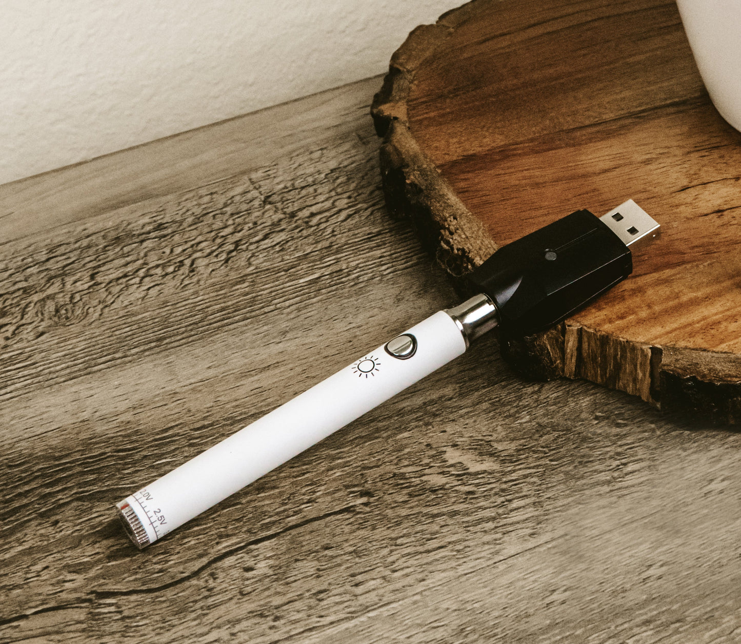 The White Jane West Day battery and its geometric USB charger laid flat on a natural wood table. This shot showcases the contrast between the modern device and organic textures, highlighting its compact portability.