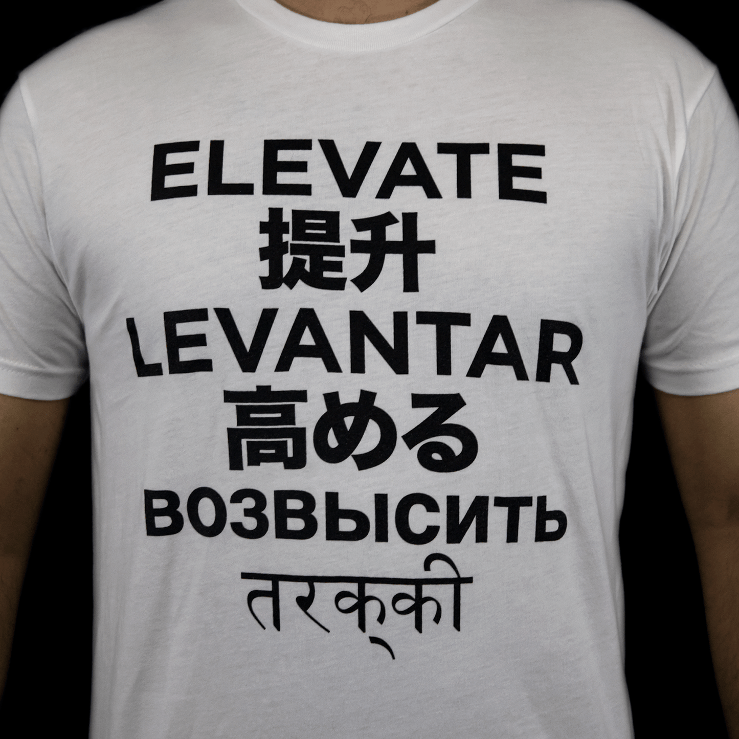 Close-up of the front chest graphic on the MJ Arsenal Elevate T-shirt showing text translations stacked in black font.
