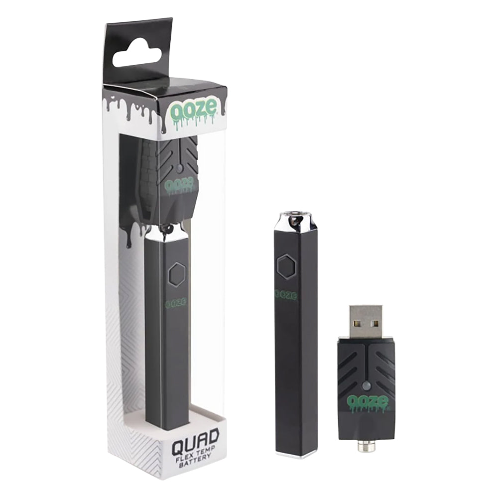A clean studio product shot featuring the Ooze Quad Flex Temp square vape pen in Panther Black. The sleek, matte black hardware stands upright next to its official clear retail display box, showing off its anti-roll flat-sided square design alongside the included black top-mounting USB charger.