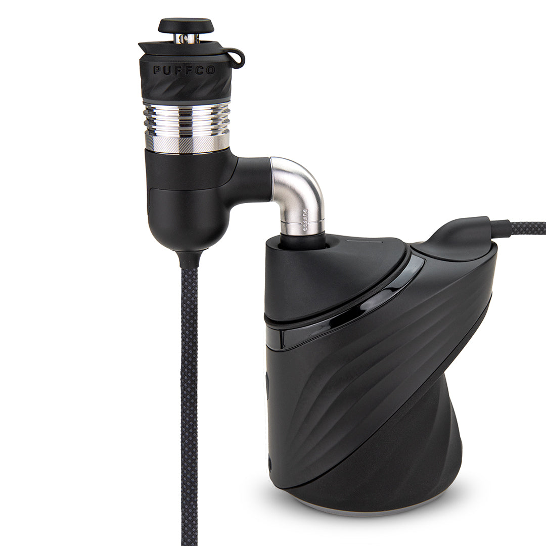 A clear, full-profile studio product shot displaying the Puffco Peak Pro Link connected directly to the Puffco Peak Pro base unit. The image illustrates how the specialized adapter module locks into the top glass/chamber connection port of the black Peak Pro base, with the tether cable extending outward to power the remote banger assembly.