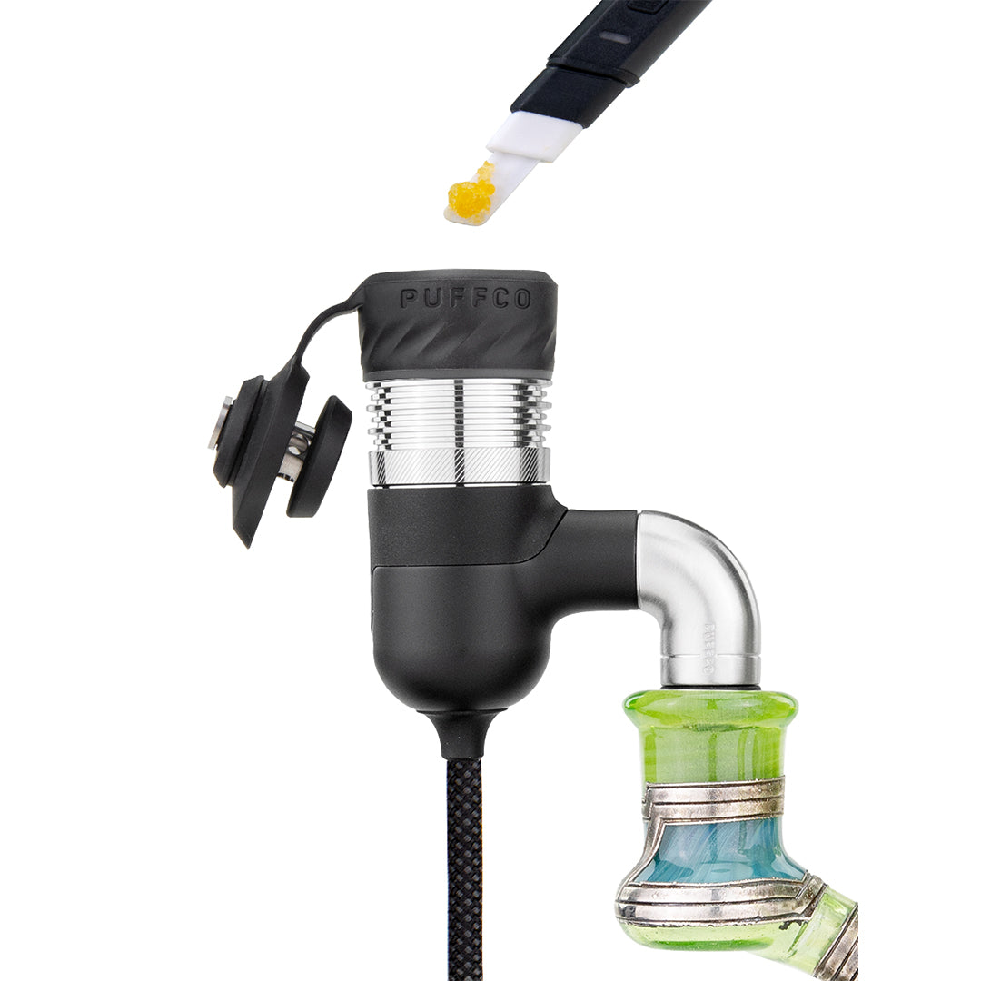 A detailed close-up action shot capturing a Puffco Hot Knife loading wax concentrate directly into the 3D chamber attached to the Peak Pro Link. The perspective focuses on the open heating element sitting atop the glass rig joint, demonstrating precise, mess-free concentrate loading in real time.