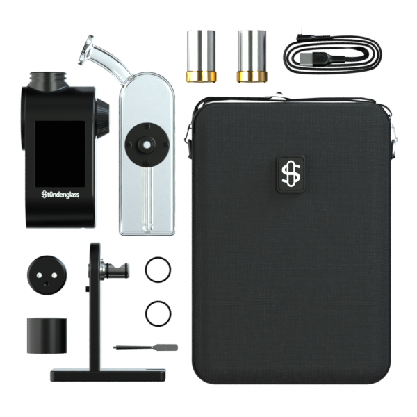 A comprehensive, top-down studio layout shot displaying the entire Stündenglass Modül + Dok Deluxe Travel Set with Clear Glass. The open hardshell carrying case sits at the top, flanked by the assembled Dok station with its clear glass globe, the digital Modül battery unit, both dry material and quartz concentrate heating tanks, the magnetic connection rings, a metal loading tool, and the USB-C fast-charging cable spread neatly on a clean background.