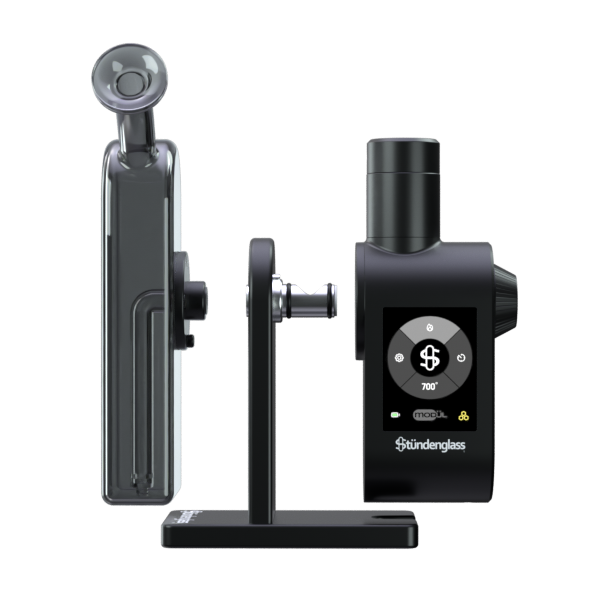 A detailed, front-facing studio demonstration shot highlighting the modular assembly of the Stündenglass Modül + Dok Deluxe Travel Set. The anodized aluminum Dok handle stands in the center, clearly showing the open magnetic side port where the compact digital Modül power unit slides in, and the top screw-threaded collar where the smoky gray borosilicate glass globe downward-stem piece securely attaches.