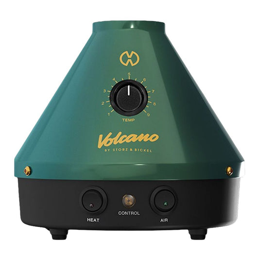 A crisp, front-facing product shot of the Storz & Bickel Volcano Classic Vaporizer 25-Year Green & Gold Limited Edition. The iconic cone-shaped desktop device features a rich matte emerald green finish, accented beautifully by a gleaming gold mechanical control dial, a gold central brand plate, and bold orange illuminated power buttons on a clean studio background.