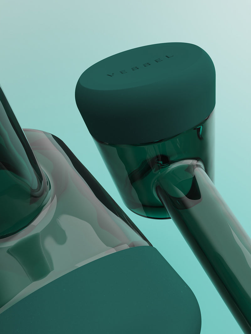 Two Vessel Forge Emerald pipes shown together for detail. One pipe provides a close-up of the glass-to-silicone seam, highlighting the precision fit of the protective base, while the second pipe is angled to show the underside, emphasizing the stability and surface-grip of the emerald silicone.