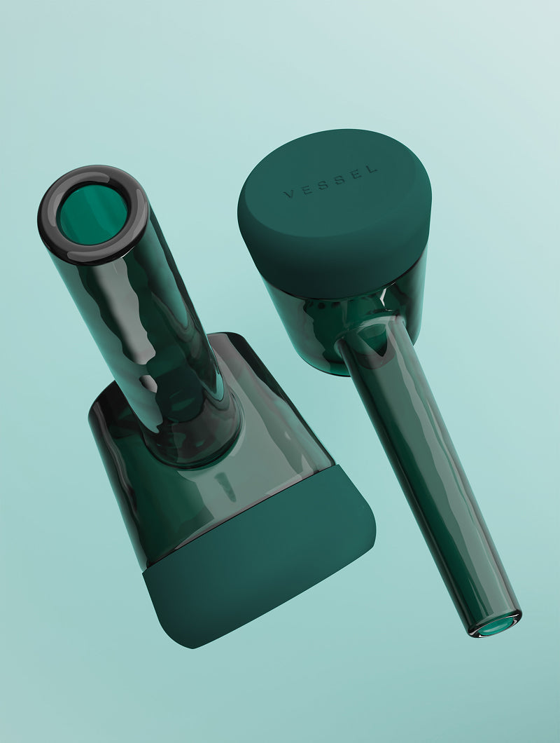 A pulled-back duo shot of two Vessel Forge Emerald pipes. One pipe is shown in a full side profile, highlighting its elegant, ergonomic silhouette, while the other is angled to show the underside of the protective emerald silicone base, demonstrating the pipe's sturdy and weighted design.